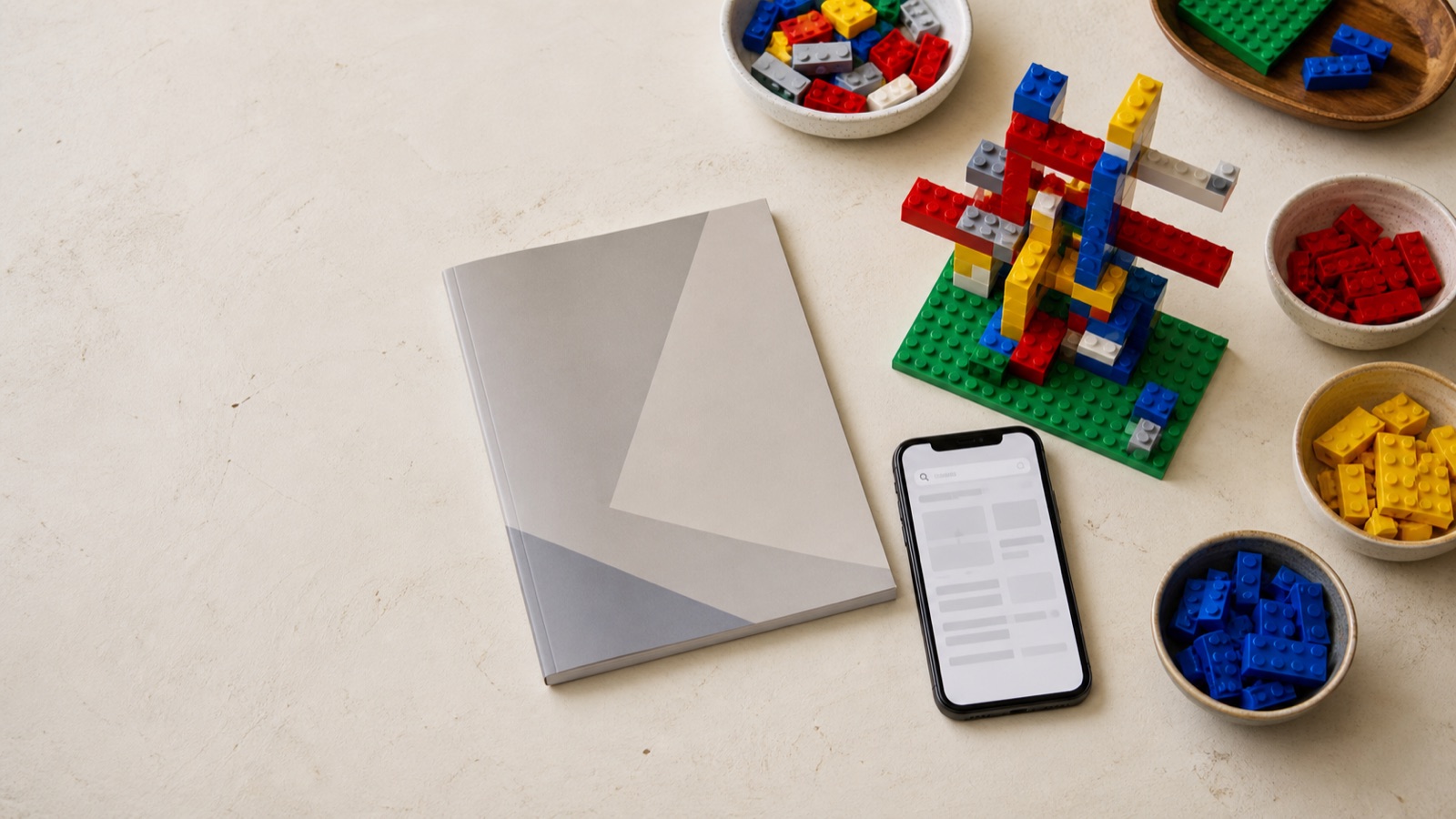 Colorful interlocking bricks, a blank instruction booklet, and a phone arranged on a building table